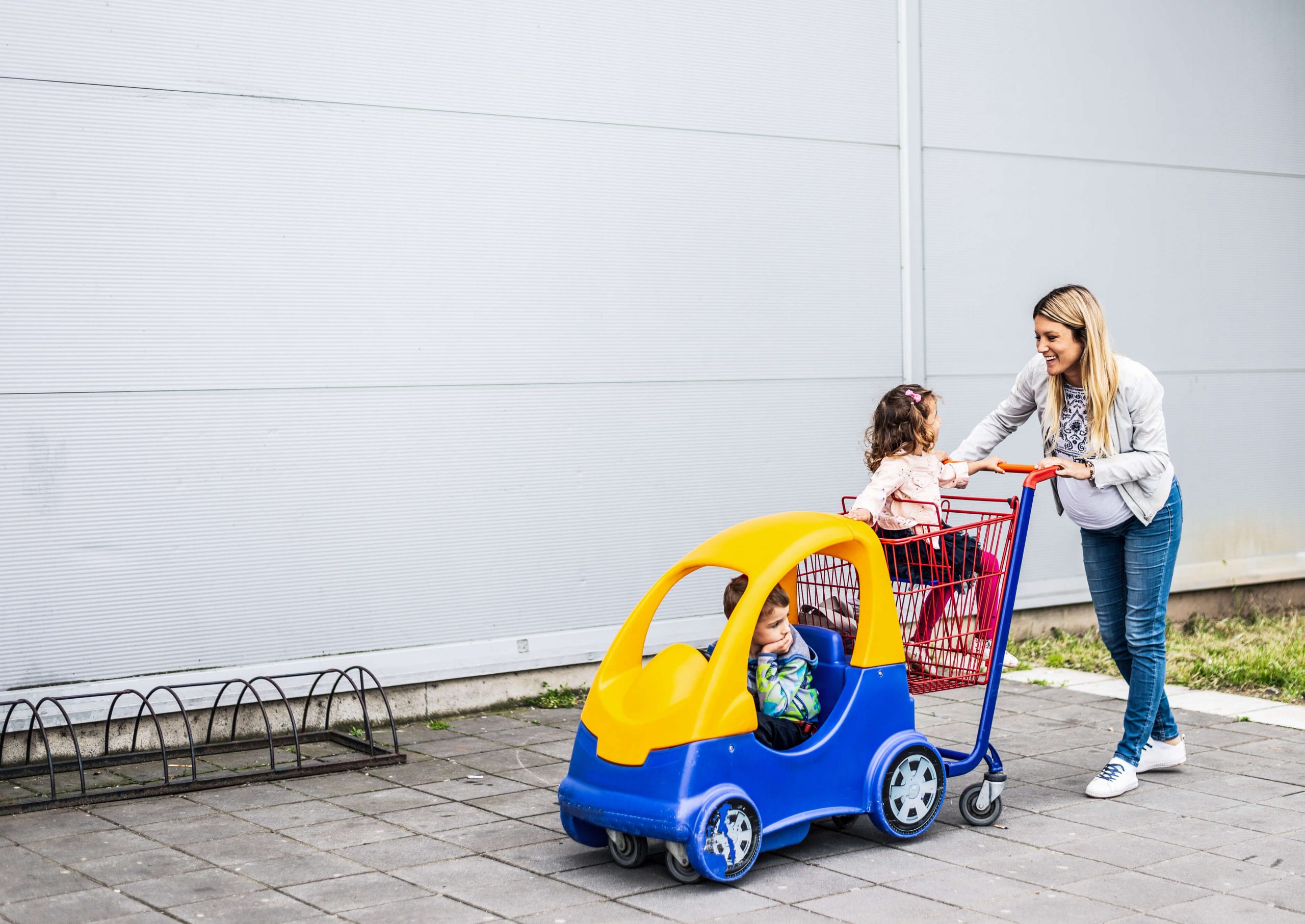 mother pushing her two children in a car themed grocery cart